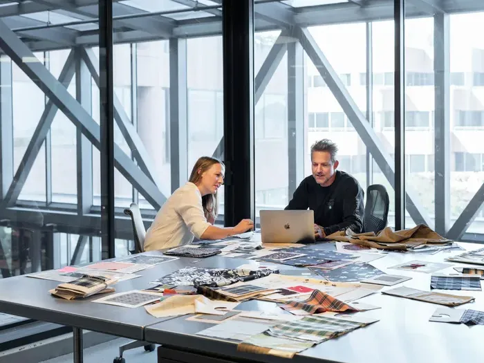 Colleagues collaborating at a large table with fabric samples and plans, showing City Connect Directory businesses